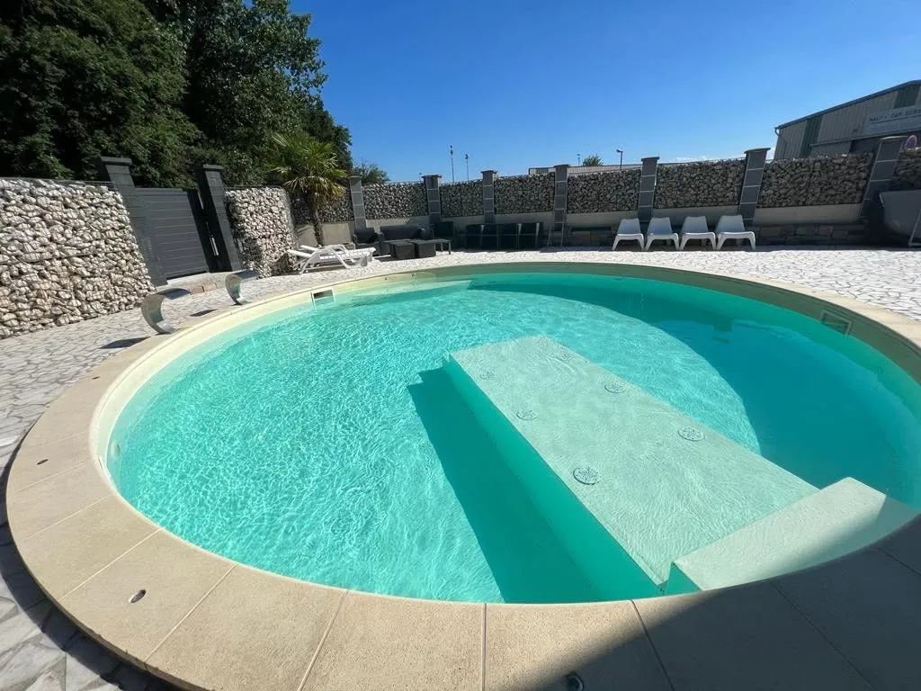 Piscine extérieure ronde à l'eau turquoise, transats et terrasse au soleil